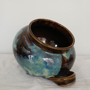 Peut inclure: Un pot en céramique brun et bleu avec un glaçage unique. Le pot a une large ouverture et un petit bec verseur sur le côté.