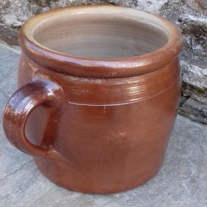 Peut inclure: Un pot en céramique brun avec une seule anse. Le pot a une large ouverture et un corps arrondi.
