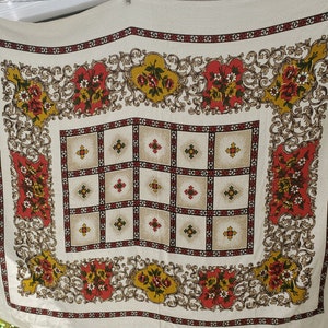 May include: A white tablecloth with a red, yellow, and green floral pattern. The tablecloth has a checkered pattern in the center and a border of floral designs.