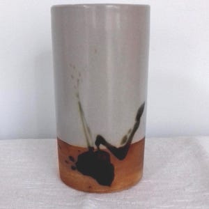 May include: A ceramic vase with a light gray glaze and a brown band around the bottom. The vase has a black abstract design on the brown band.