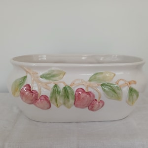 Peut inclure: Pot en céramique blanche avec un motif en relief de feuilles vertes et de cerises roses.