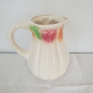 May include: A white ceramic pitcher with a textured surface and a floral design in shades of green, pink, and orange.