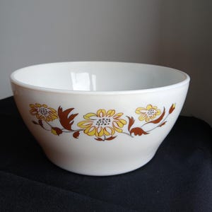 Może przedstawiać: Biała ceramiczna miska z kwiatowym wzorem. Kwiaty są żółte i brązowe, z zielonymi liśćmi. Miska jest okrągła i ma szeroki otwór. Miska jest prawdopodobnie vintage i nadaje się do serwowania.