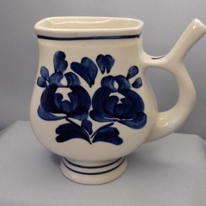 Puede incluir: Jarra de cerámica blanca con un diseño floral azul y un pico. La jarra tiene un asa y una base.