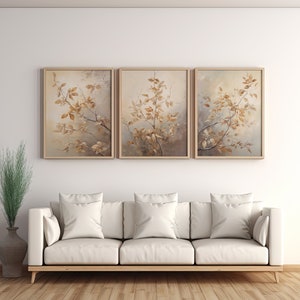May include: Three framed prints of a watercolor painting of a branch with brown leaves against a light gray background. The prints are hanging on a white wall above a white couch with three white pillows.