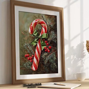 May include: A framed print featuring a candy cane with red and white stripes, a green bow, and red berries, set against evergreen branches. The artwork is displayed on a wooden surface.