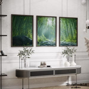 May include: Three framed prints of a misty green bamboo forest with a path leading through the center. The prints are hung on a white wall above a modern console table.