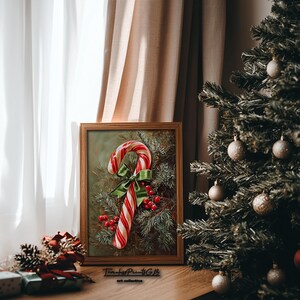 May include: A framed print featuring a candy cane with red and white stripes, a green bow, and red berries. The artwork is set against a backdrop of evergreen branches. The print is displayed near a Christmas tree.