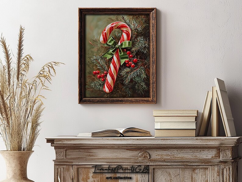 May include: A framed print of a candy cane with red and white stripes, a green bow, and red berries. The artwork is set against evergreen branches. The frame is dark brown. The print is displayed on a white wall, above a wooden cabinet.