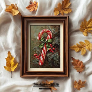 May include: A framed print depicting a red and white striped candy cane with a green bow and red berries, set against evergreen branches. The artwork is in a brown wooden frame, with autumn leaves scattered around.