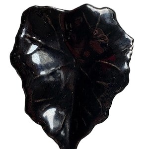 May include: A glossy black ceramic leaf-shaped dish. The dish has detailed veining and a slightly curved shape. The dark color and organic form suggest a decorative or serving piece, suitable for a modern or nature-inspired aesthetic.