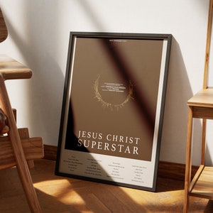 May include: A framed poster with a brown background and gold accents. The poster features the title "Jesus Christ Superstar" and a list of songs from the musical.