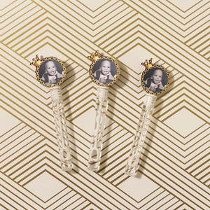May include: Three clear plastic bubble wands with gold crowns and a photo of a young boy in a black and white photo. The photo is in a round frame with a gold chain border.