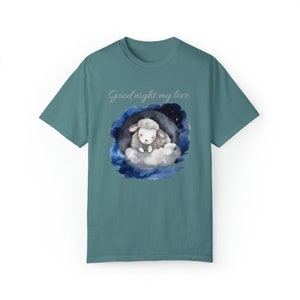 May include: A teal blue t-shirt featuring a watercolour illustration of a sleeping lamb on a cloud in a starry night sky. The text "Good night my love" is printed above the illustration.