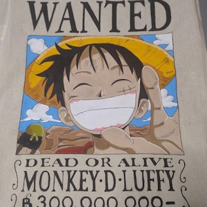 Peut inclure: Sac fourre-tout beige avec une illustration colorée de Monkey D. Luffy de One Piece. L'image comprend le texte "WANTED" en haut, et "DEAD OR ALIVE" et "MONKEY D. LUFFY" en dessous de l'illustration.