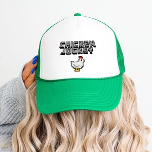 May include: A white and green trucker hat with a pixelated chicken and the text "Chicken Jockey" on the front.