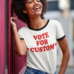 May include: A white t-shirt with a black ringer and red text that says "VOTE FOR *CUSTOM*"