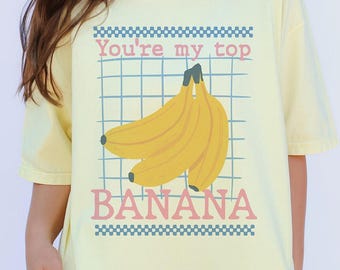 May include: A yellow t-shirt with a graphic of bananas and the text "You're my top banana" in pink and blue.