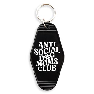 May include: Black motel key chain with the text "Anti Social Dog Moms Club" in white lettering. The key chain features a paw print graphic.