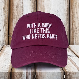May include: Burgundy baseball cap with white embroidered text that reads "With a body like this who needs hair?"