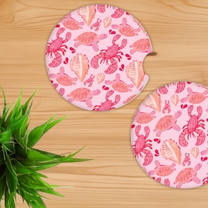 May include: Two pink round coasters with a repeating pattern of pink and orange sea turtles, seashells, and crabs.