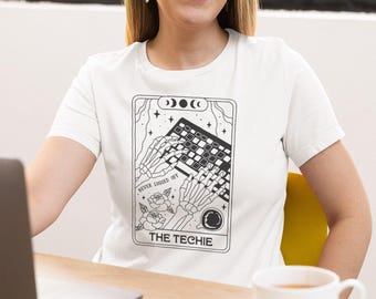 May include: White t-shirt featuring a black and white graphic of skeleton hands typing on a keyboard. The graphic includes the text "NEVER LOGGED OFF" and "THE TECHIE". The design is framed with stars, moons, and roses.