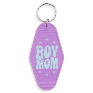 May include: A purple motel-style keychain with the words "BOY MOM" in light blue, surrounded by starburst graphics. The keychain has a silver metal ring at the top for attaching keys.