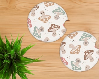 May include: Two round car coasters with a whimsical mushroom pattern. The coasters feature a cream background with smiling mushrooms in shades of brown, pink, and green. One coaster has a notch for easy removal from the car cup holder.