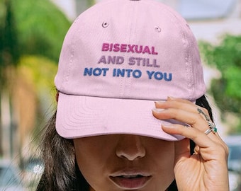 May include: Pink baseball cap with the text "Bisexual and Still Not Into You" embroidered in pink, blue, and purple.