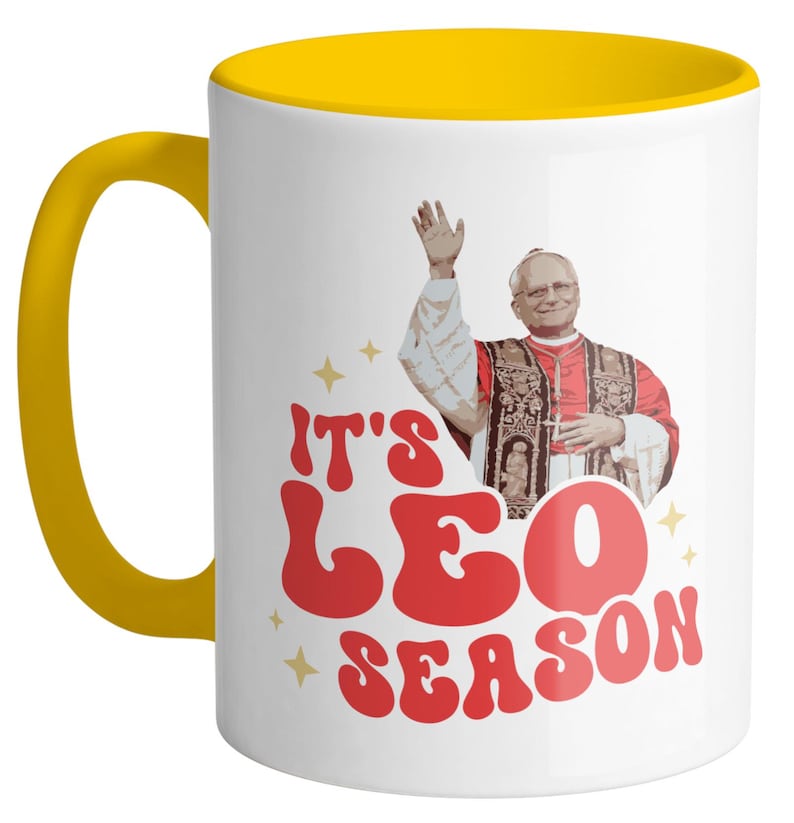 May include: White ceramic mug with a yellow rim. The mug features a retro-style graphic of a man in a red robe with the text "It's Leo Season".