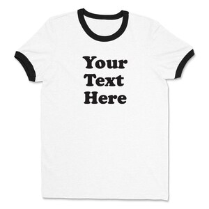 May include: White t-shirt with black ringer sleeves and the text "Your Text Here" printed in black.