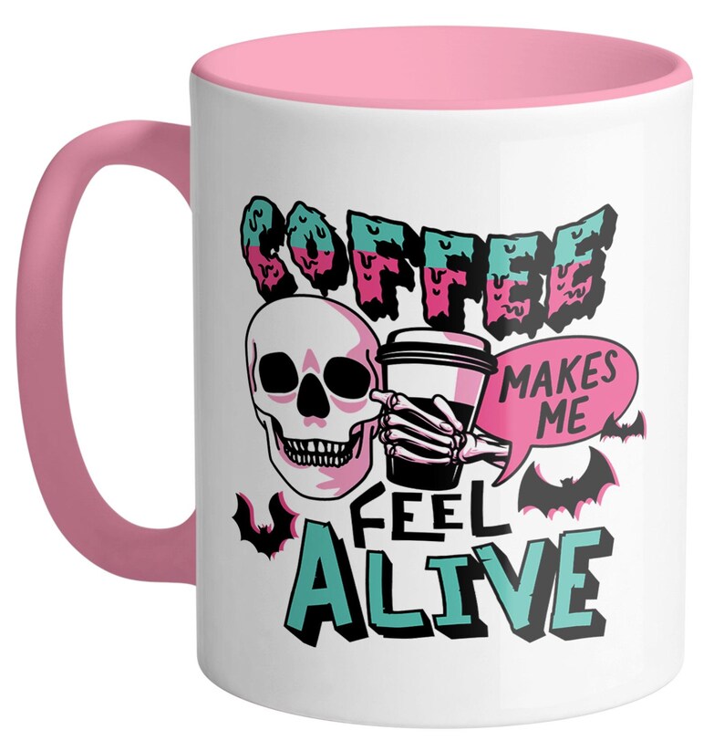 May include: White ceramic coffee mug with a pink interior and handle. The mug features a skull graphic holding a coffee cup, with the words "COFFEE MAKES ME FEEL ALIVE" in a spooky font. Bats are also included in the design.
