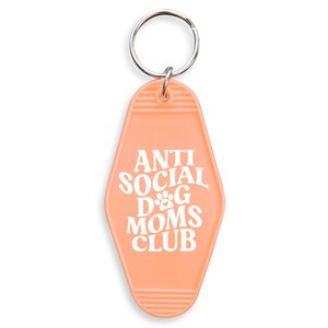 May include: Peach-colored motel key chain with the text "Anti Social Dog Moms Club" in white. The keychain has a silver key ring.