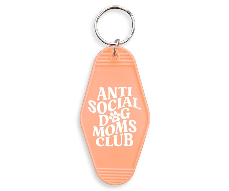 May include: Peach-colored motel key chain with the text "Anti Social Dog Moms Club" in white. The keychain has a silver key ring.