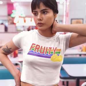 May include: White cropped t-shirt with a rainbow stripe design and the word "FRUITY" in red letters. Two yellow lemons are below the text.