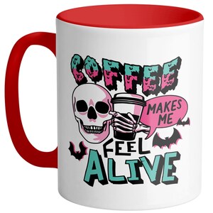 May include: White ceramic coffee mug with a red handle and interior. The mug features a skull graphic holding a coffee cup, with the words "COFFEE MAKES ME FEEL ALIVE" in a spooky font. Bats are also included in the design.