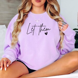 May include: A lavender sweatshirt with the text "Let them" and a small heart in black.