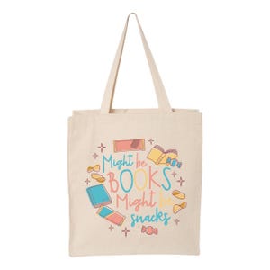 May include: A beige tote bag with a colourful design featuring the text "Might be BOOKS Might be snacks" and illustrations of books, snacks, and stars.