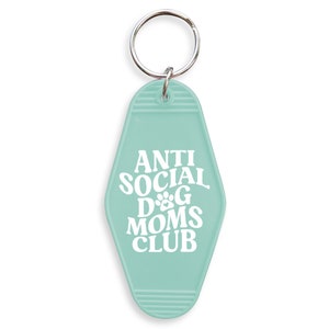 May include: A light blue key chain with a motel key tag design. The key tag has white text that reads "Anti Social Dog Moms Club".