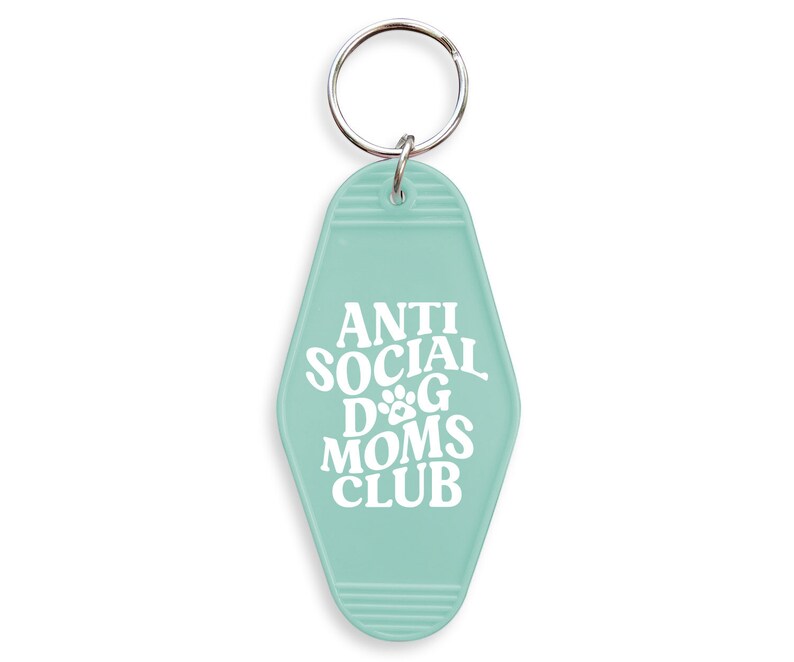 May include: A light blue key chain with a motel key tag design. The key tag has white text that reads "Anti Social Dog Moms Club".