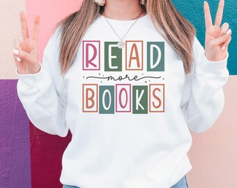 May include: White sweatshirt with the text "READ more BOOKS" in colorful block letters.