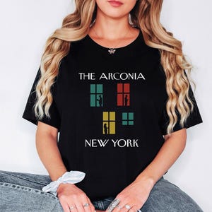 May include: Black t-shirt with the text "THE ARCONIA NEW YORK" and a graphic of three windows with silhouettes of people inside.
