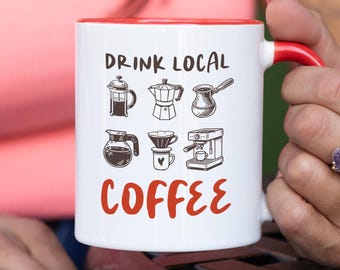 May include: White coffee mug with a red interior and handle. The mug features the text "DRINK LOCAL COFFEE" in black and red, along with illustrations of various coffee brewing methods.