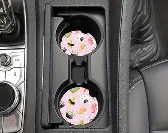 May include: Two car coasters with a pink background and a pattern of sushi rolls, nigiri, and other sushi items. The coasters are in a car's cup holders, with the car's interior visible.