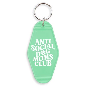 May include: A light green key chain with a silver key ring. The key chain is shaped like a motel key and has the text "ANTI SOCIAL DOG MOMS CLUB" in white.