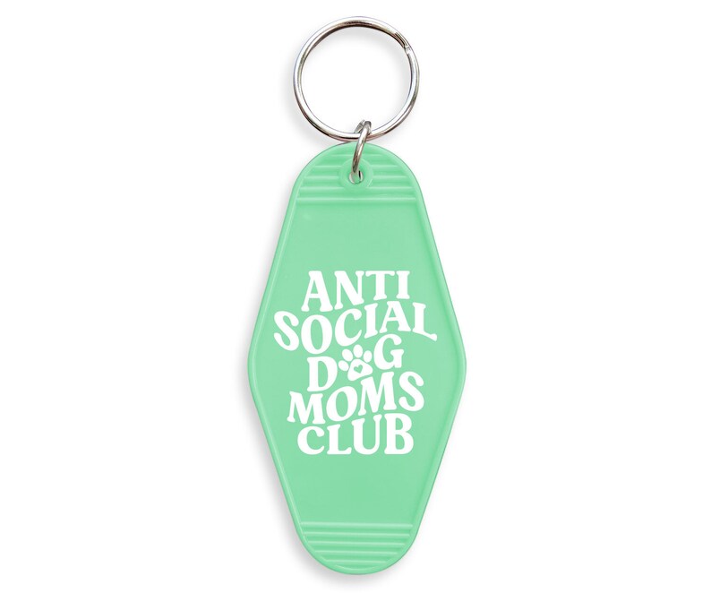 May include: A light green key chain with a silver key ring. The key chain is shaped like a motel key and has the text "ANTI SOCIAL DOG MOMS CLUB" in white.