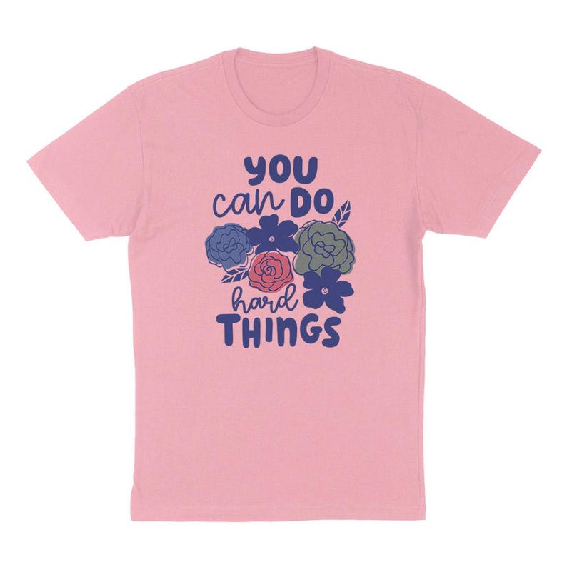 Puede incluir: Camiseta rosa claro con el texto "YOU can DO hard THINGS" en azul y blanco. El dise&ntilde;o incluye ilustraciones florales en azul, rojo y verde.