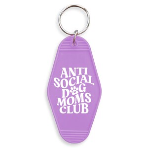 May include: Purple motel key chain with the text "Anti Social Dog Moms Club" in white lettering. The key chain has a paw print in the text.
