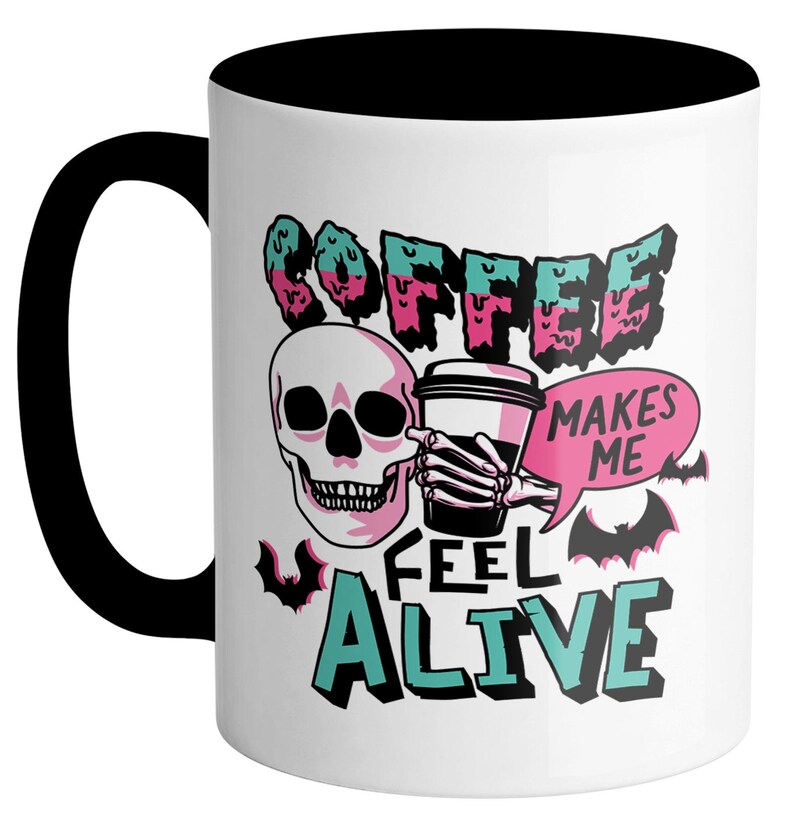 May include: White ceramic coffee mug with a black handle and interior. The mug features a skull graphic holding a coffee cup, with the words "COFFEE MAKES ME FEEL ALIVE" in a teal, pink, and black design.