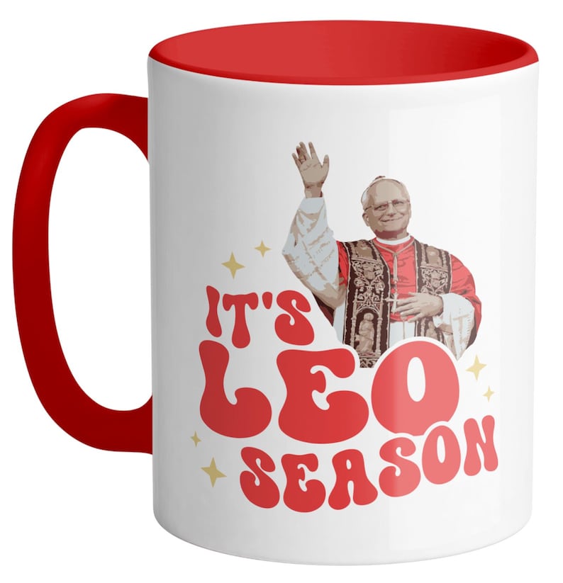 May include: White ceramic coffee mug with a red rim. The mug features a retro-style graphic of a man in a red robe with the text "It's Leo Season".